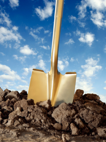 Gold shovel in freshly dug dirt with blue sky